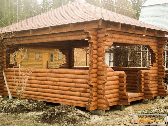 A wooden frame is the most suitable material for making an arbor for an infield in the style of a chalet. The roof made of terracotta tiles looks organically on the background of an aged tree.